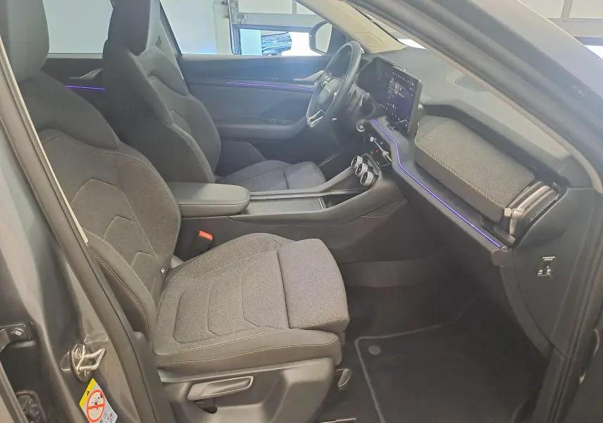 Vue intérieure côté conducteur du Skoda Kodiaq gris graphite 2025, avec sièges tissu et éclairage d'ambiance violet sur la planche de bord.
