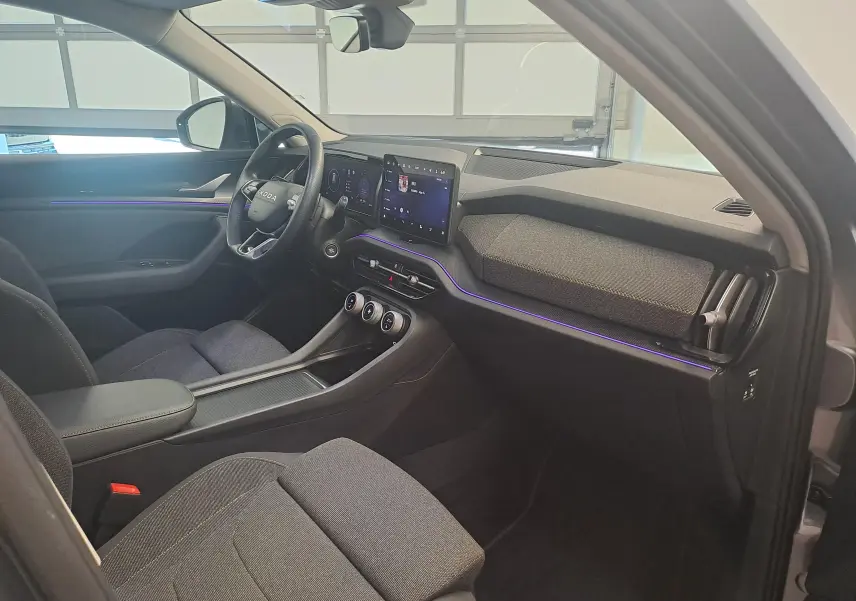 Intérieur du Skoda Kodiaq 2025 vu côté conducteur, tableau de bord moderne avec éclairage d'ambiance violet et sièges gris.