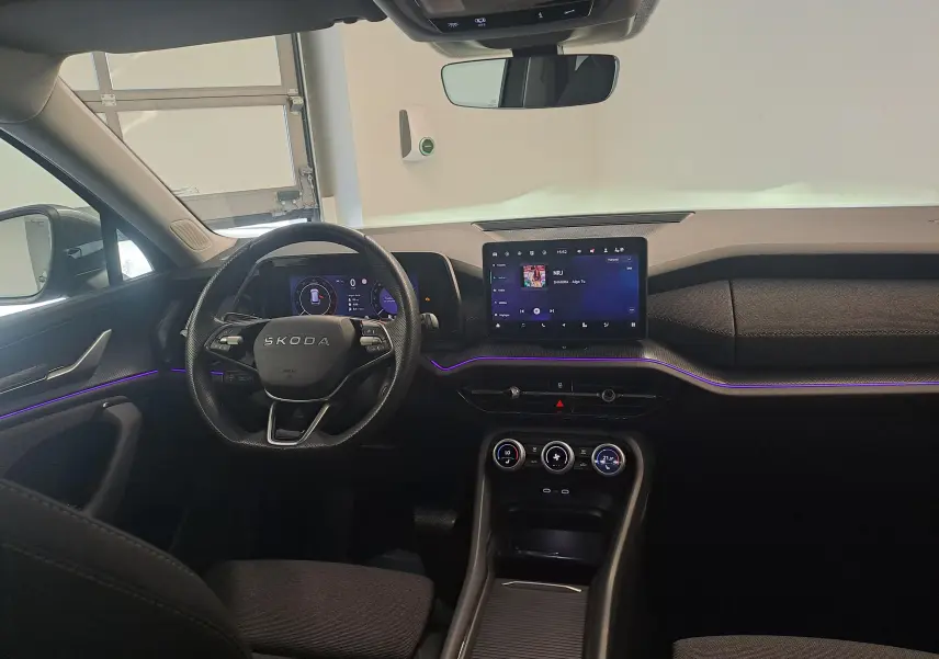 Vue intérieure avant du Skoda Kodiaq 2025, tableau de bord noir avec éclairage d'ambiance violet et écran tactile central.
