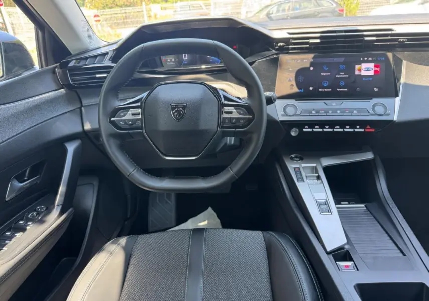 Vue intérieure de face du poste de conduite gris de la Peugeot 308 2025 avec volant multifonction et écran tactile central.