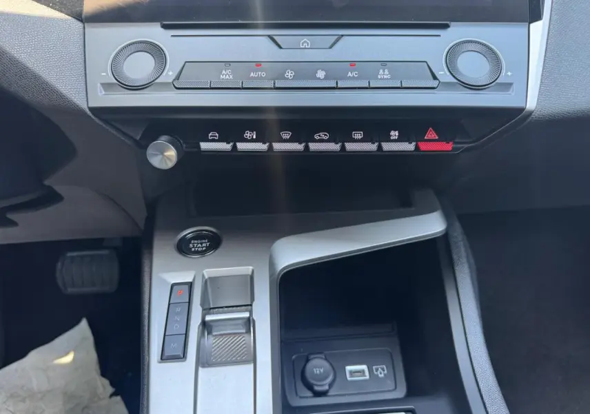 Vue rapprochée du tableau de bord et console centrale grise de la Peugeot 308 2025 avec commandes climatisation et levier de boîte auto.