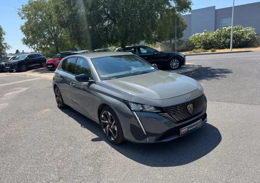 Peugeot 308 gris vue 3/4 avant droit, avec jantes alliage 17 pouces et calandre noire distinctive.