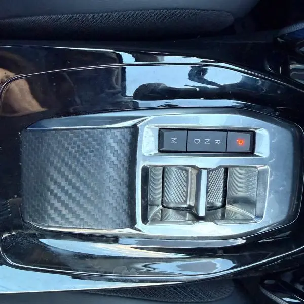 Vue plongeante sur la console centrale noire du Peugeot 208 Hybrid 110, avec levier de vitesses automatique et finition carbone.