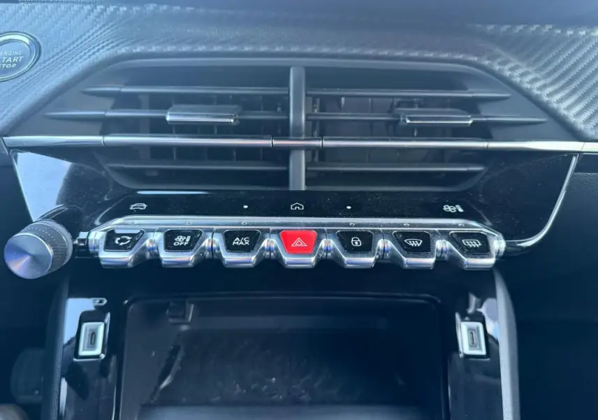 Vue rapprochée du tableau de bord noir de la Peugeot 208 Hybrid 110, montrant les commandes centrales et la grille d’aération.