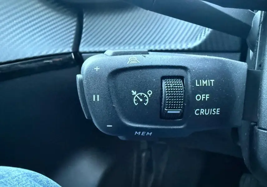 Gros plan sur la commande de régulateur de vitesse du Peugeot 208 Hybrid 110 e-DCS6 Allure, intérieur noir.