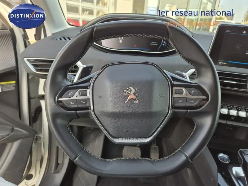 Vue rapprochée du volant cuir noir multifonction d’un Peugeot 3008 blanc nacré, avec tableau de bord numérique en arrière-plan.