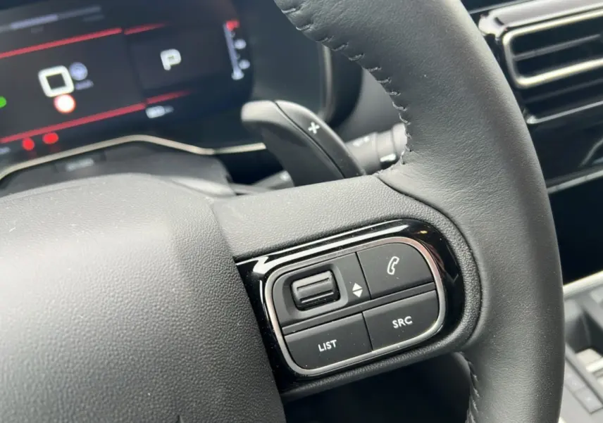 Gros plan sur le volant cuir noir du Citroën C5 Aircross Hybrid 145, avec commandes multifonctions et palettes au volant visibles.