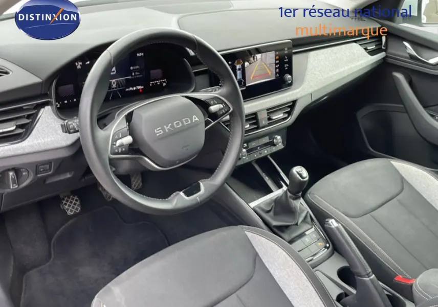 Vue intérieure de la Skoda Scala 2025 montrant le tableau de bord, volant cuir, écran central et sièges tissu gris noir.