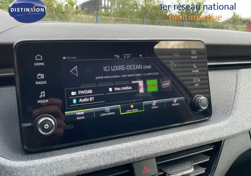 Écran tactile central du tableau de bord de la Skoda Scala blanc glacier, affichant la radio FM/DAB et Bluetooth.
