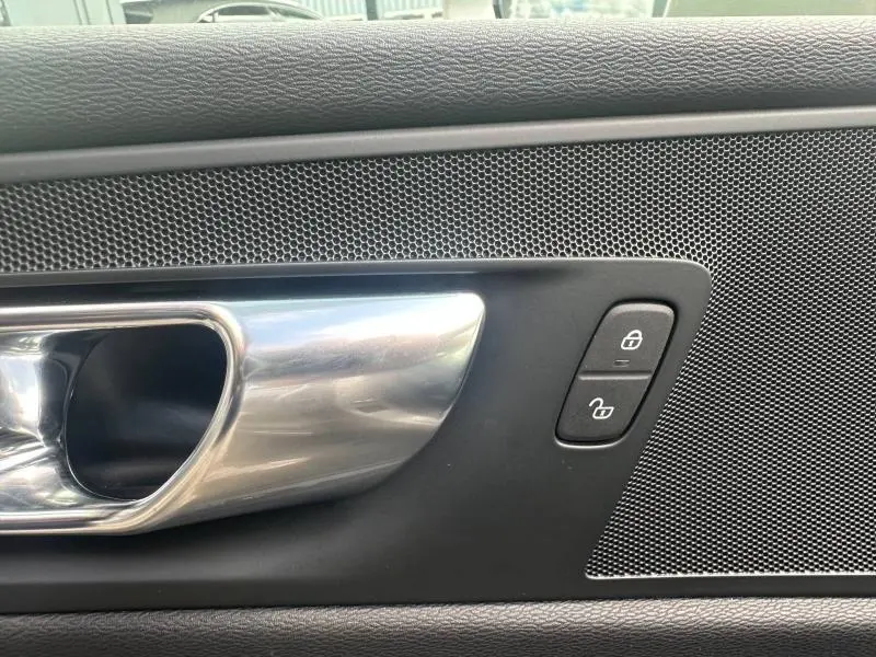 Poignée de porte intérieure chromée côté gauche avec boutons de verrouillage et haut-parleur noir sur Volvo XC60 gris 2024.