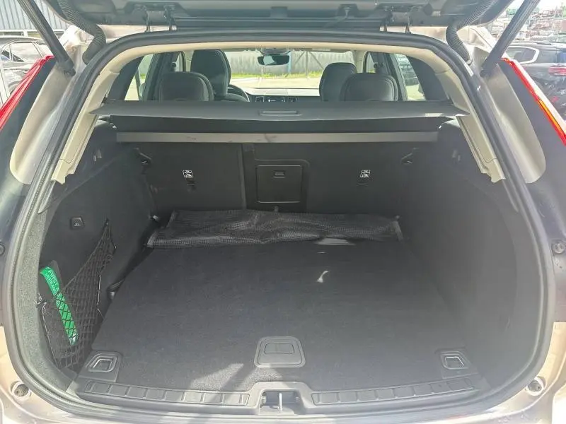 Coffre ouvert vu de l'arrière d'un Volvo XC60 gris, montrant un espace de chargement propre avec filet de rangement latéral.