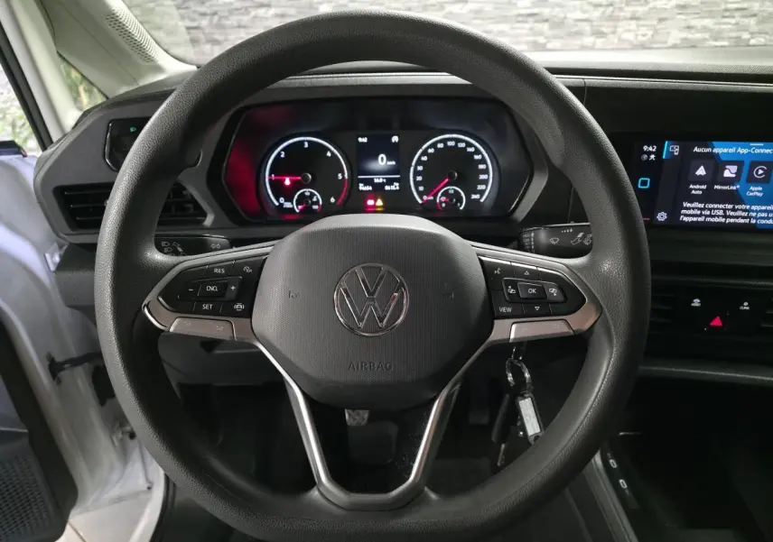 Vue rapprochée du volant multifonction noir et du tableau de bord numérique du Volkswagen Caddy Cargo blanc 2023.