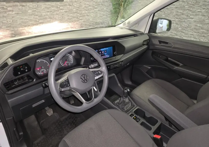 Vue intérieure côté conducteur du Volkswagen Caddy Cargo blanc 2023, avec tableau de bord noir et volant multifonction.
