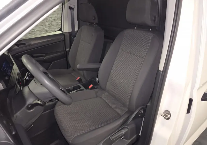Vue intérieure côté conducteur du Volkswagen Caddy Cargo blanc 2023, sièges tissu gris avec accoudoir et planche de bord noire.