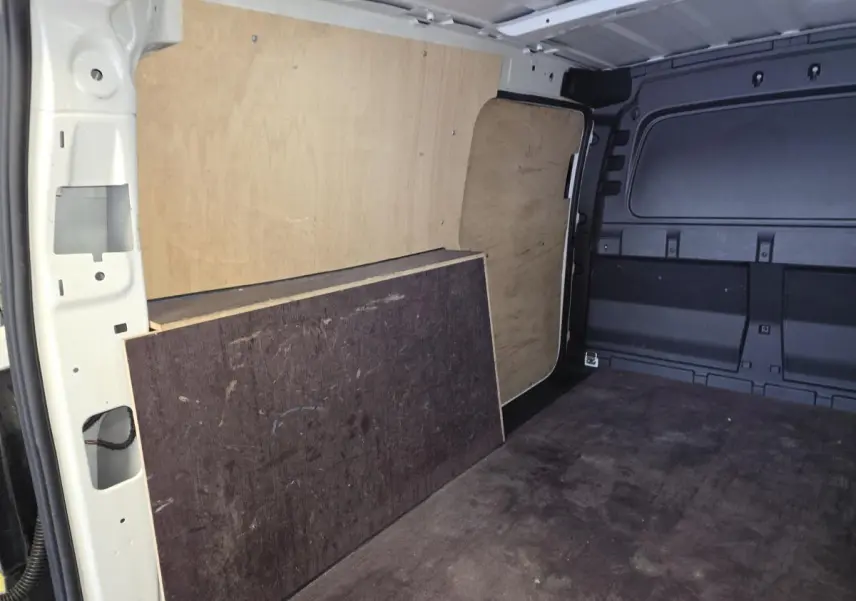Vue intérieure du compartiment de charge du Volkswagen Caddy Cargo blanc, avec revêtement bois et caoutchouc au sol.