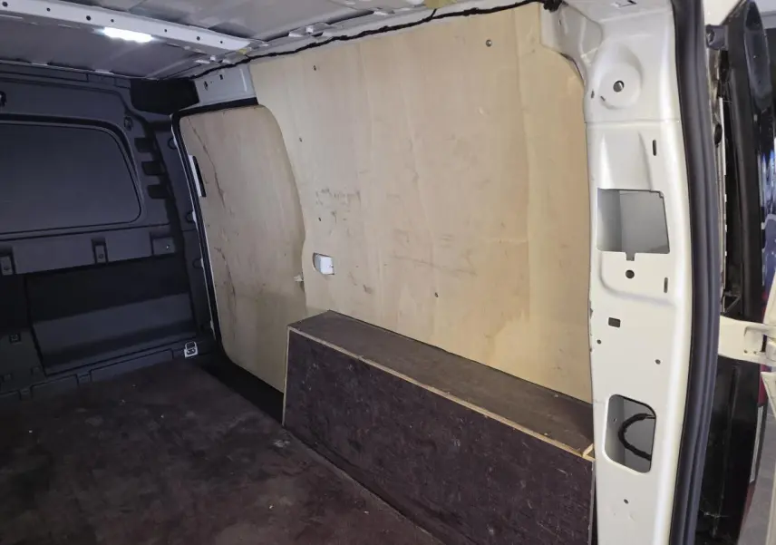 Vue intérieure du compartiment de charge du Volkswagen Caddy Cargo blanc, avec revêtement bois et tapis caoutchouc au sol.