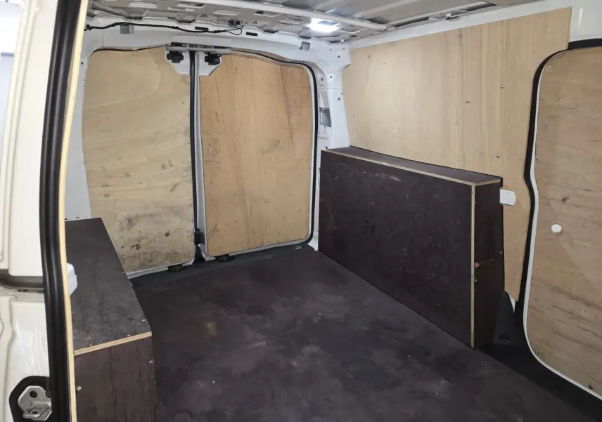 Vue intérieure arrière du fourgon blanc Volkswagen Caddy Cargo 2023, montrant le compartiment de charge avec revêtement bois.