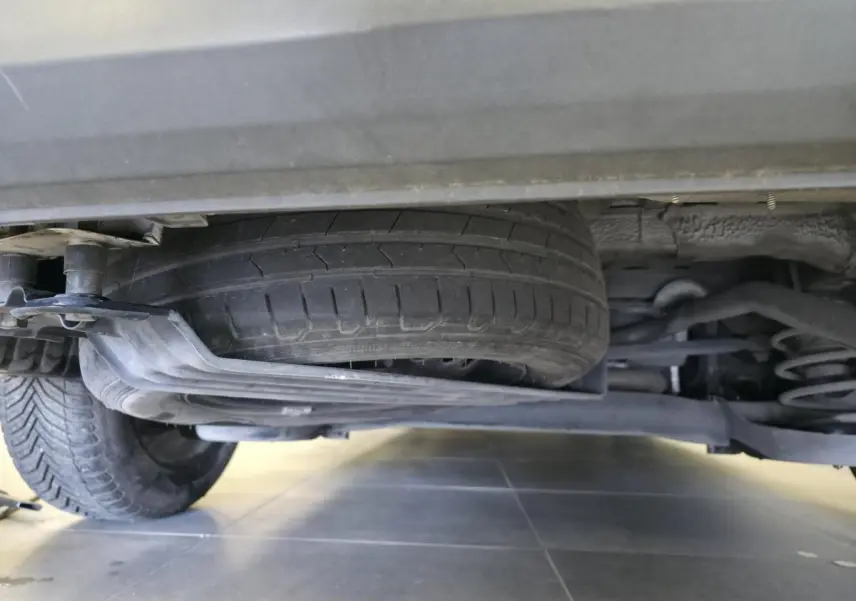 Vue en contre-plongée sous un Volkswagen Caddy blanc montrant la roue de secours et la suspension arrière.