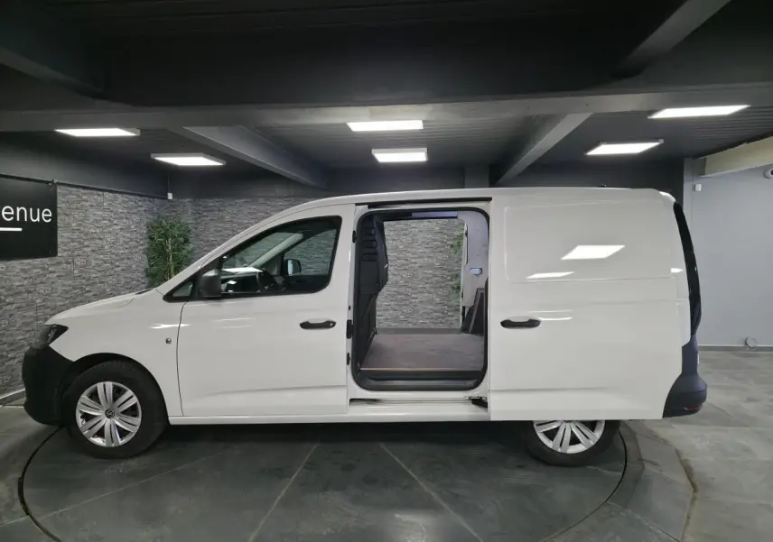 Vue de profil droit d’un utilitaire Volkswagen Caddy Cargo blanc avec porte coulissante ouverte sur le compartiment de charge.
