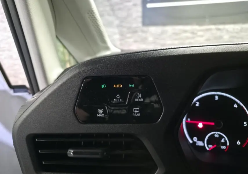 Détail du tableau de bord noir mat du Volkswagen Caddy 2023 avec commandes d'éclairage et ventilation côté conducteur.