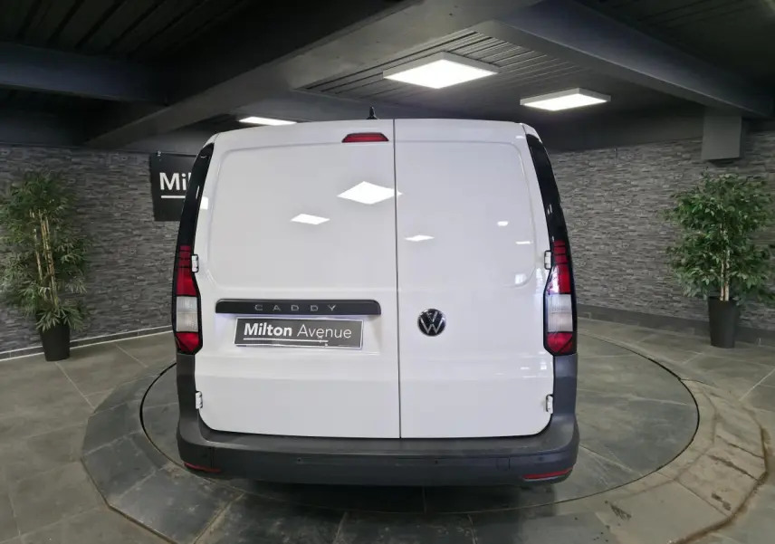 Vue arrière d'un Volkswagen Caddy Cargo blanc 2023 avec portes battantes et pare-chocs noirs dans un showroom.