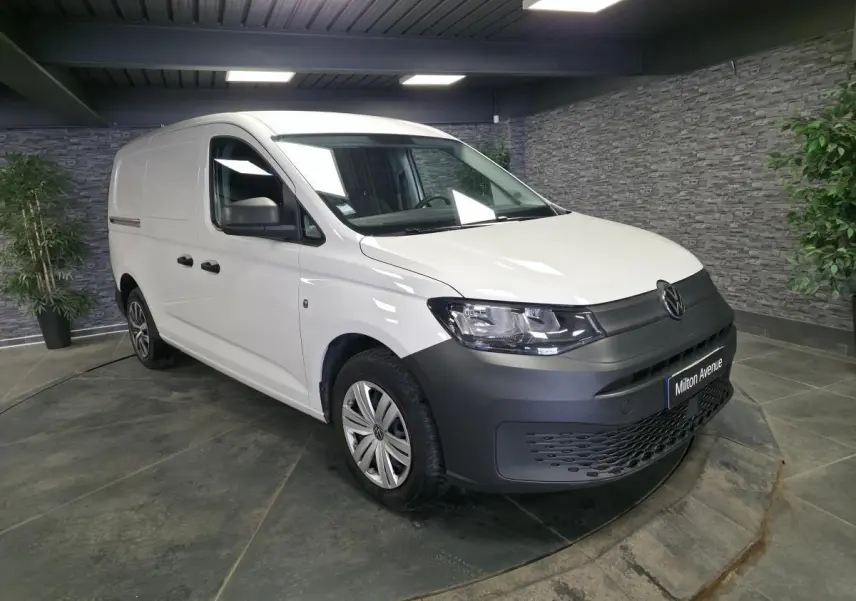 Volkswagen Caddy Cargo blanc en 3/4 avant droit avec pare-chocs noirs et jantes acier en intérieur showroom.