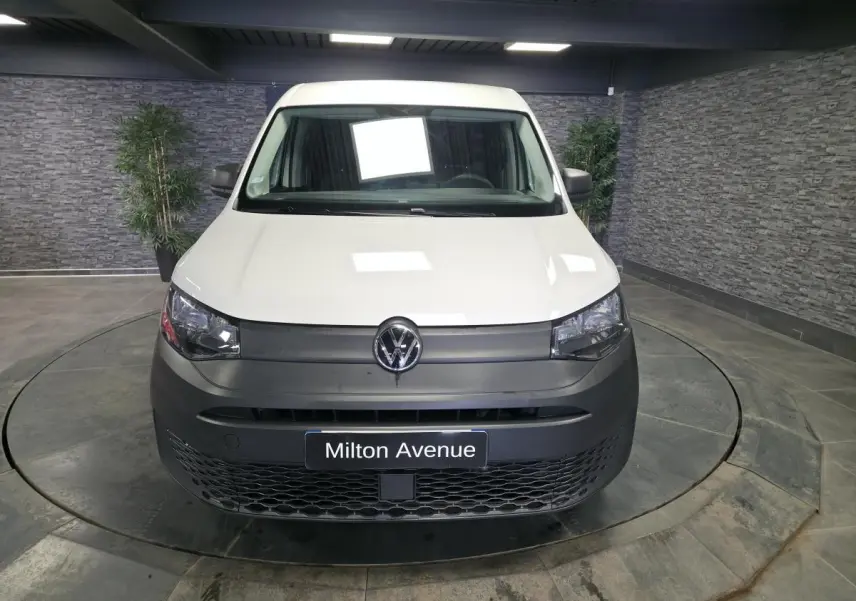 Vue avant d'un Volkswagen Caddy Cargo blanc avec pare-chocs noir mat dans un showroom intérieur.