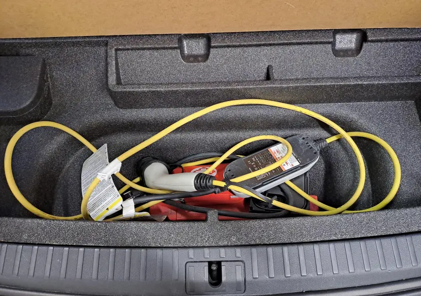 Gros plan sur le compartiment de coffre d'une Skoda Octavia Combi gris perle, montrant le câble de recharge hybride rangé.