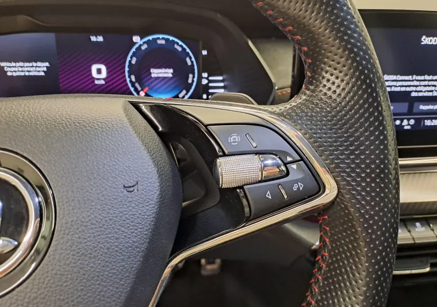 Gros plan sur le volant perforé avec surpiqûres rouges et commandes multifonctions du Skoda Octavia Combi gris perle.