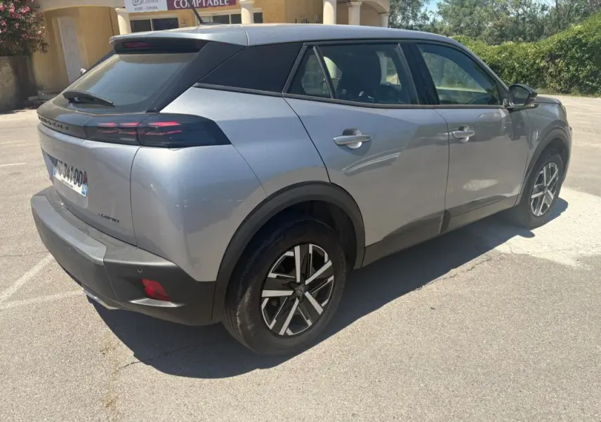 Vue 3/4 arrière droite d’un Peugeot 2008 Hybrid gris 2025 avec jantes 16 pouces et toit noir contrasté.