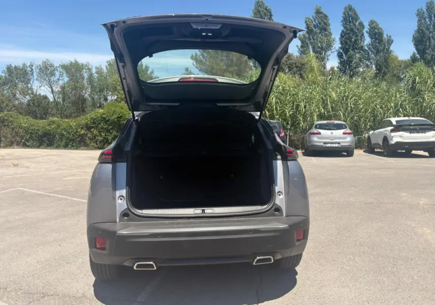 Vue arrière d’un Peugeot 2008 Hybrid gris 2025 avec coffre ouvert, double sortie d’échappement et feux LED.