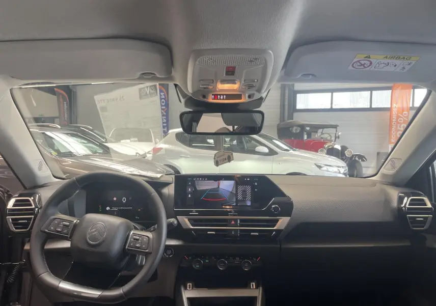 Vue intérieure avant du tableau de bord noir et volant cuir d'une Citroën C4 hybride avec écran tactile et caméra de recul affichée.