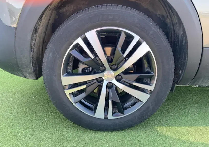 Gros plan sur la roue avant gauche du Peugeot 5008 gris Amazonite avec jante alliage bicolore moderne.