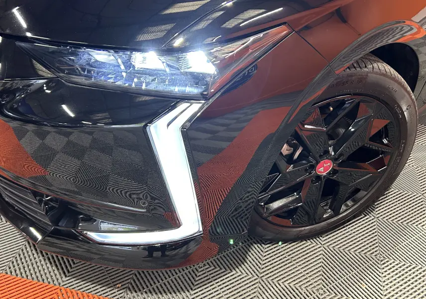 Gros plan sur l'avant droit noir Perla Nera du DS4 2024, mettant en valeur le phare LED et la jante noire à étoile rouge.