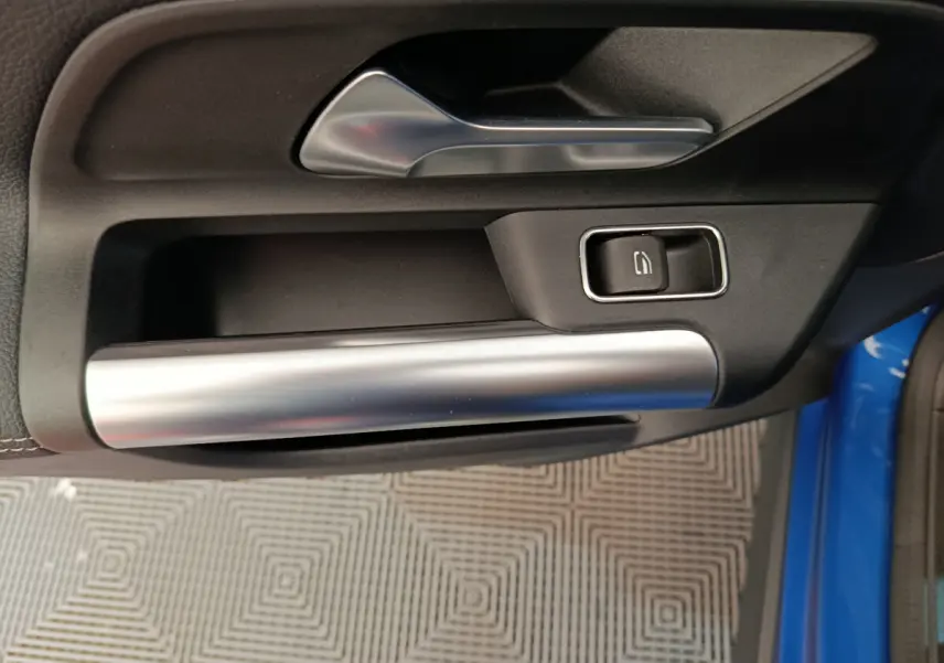 Poignée intérieure côté gauche de porte d'une Mercedes GLA 250 e Business Line bleu, avec bouton de verrouillage noir et garniture argentée.