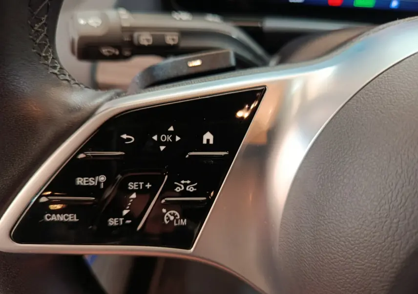 Gros plan sur les commandes multifonctions à gauche du volant cuir du Mercedes GLA 250 e Business Line bleu 2024 hybride.