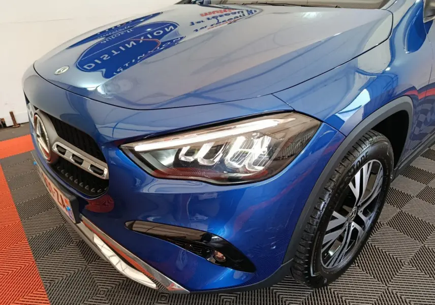 Vue 3/4 avant droit d'une Mercedes GLA 250 e Business Line hybride rechargeable bleu métallisé avec phares LED allumés.