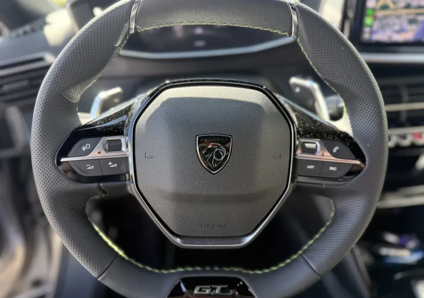 Vue rapprochée du volant cuir noir avec surpiqûres vertes et logo Peugeot sur le Peugeot 2008 Hybrid 145ch GT 2025.