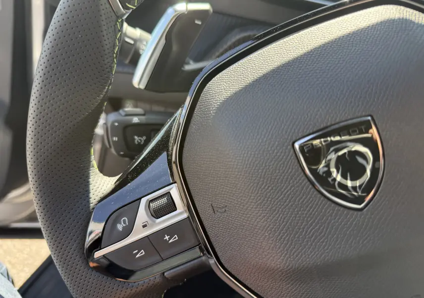 Gros plan sur le volant perforé noir du Peugeot 2008 Hybrid 145ch GT, avec logo lion chromé au centre.