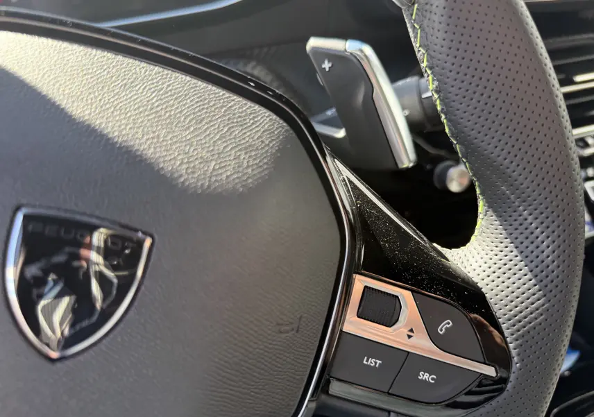 Gros plan sur le volant perforé noir du Peugeot 2008 Hybrid 145ch, avec commandes intégrées et palettes au volant.