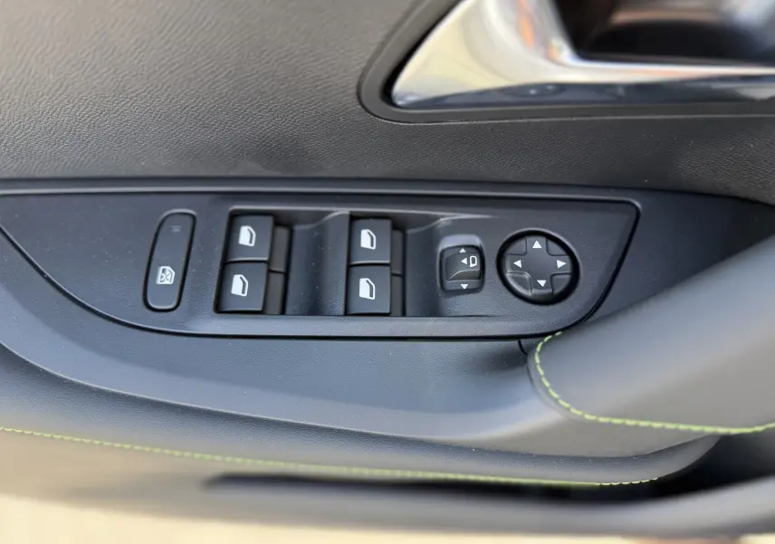 Gros plan sur les commandes des vitres et rétroviseurs côté gauche, garniture noire avec surpiqûres vertes.