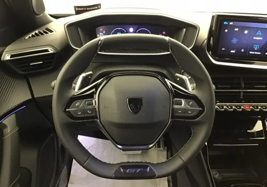 Vue frontale du volant cuir noir avec logo Peugeot et badge GT du tableau de bord du Peugeot 2008 Hybrid 2025.