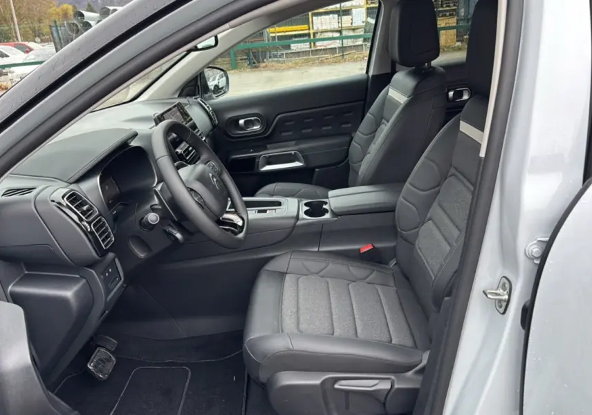 Vue intérieure côté conducteur du Citroën C5 Aircross Hybrid blanc, montrant les sièges en cuir et tissu gris et le tableau de bord moderne.