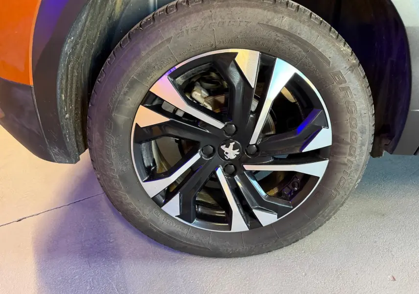 Gros plan sur la roue avant gauche d’un Peugeot 2008 orange, jante alliage bi-ton noir et argent avec logo lion central.