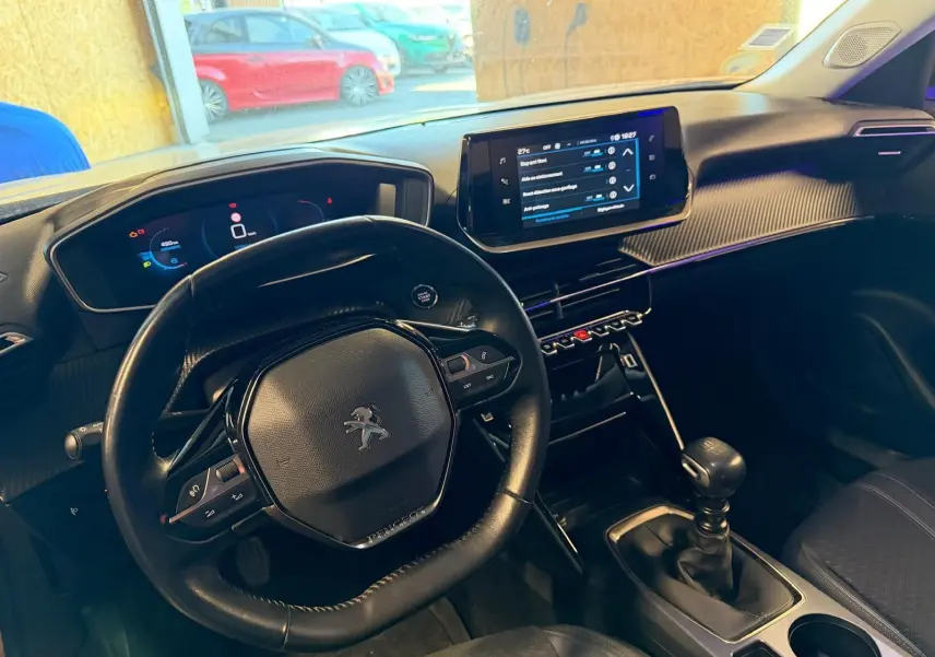 Vue intérieure de face du tableau de bord et volant compact noir du Peugeot 2008 1.5 BlueHDi 100 Allure avec écran tactile central.