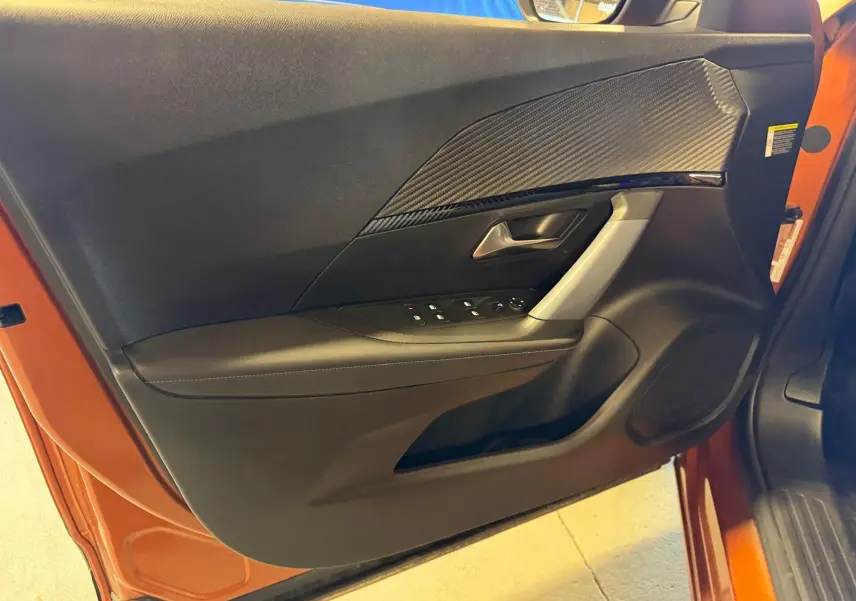Vue intérieure de la porte avant gauche orange du Peugeot 2008 1.5 BlueHDi avec insert carbone et commandes électriques.