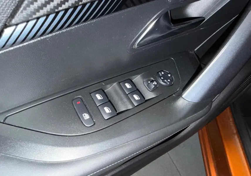 Gros plan sur la commande des vitres électriques côté conducteur dans l'intérieur noir du Peugeot 2008 orange 2020.