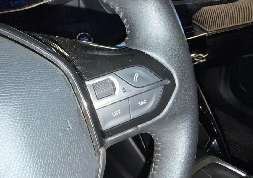 Gros plan sur le volant cuir noir du Peugeot 2008 2020 avec commandes multimédia à gauche.