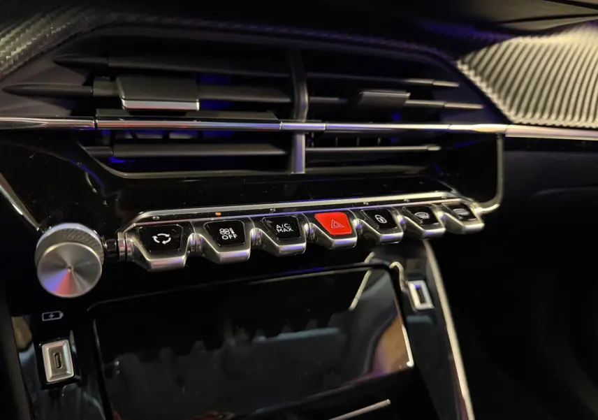 Gros plan sur la console centrale noire brillante du Peugeot 2008 1.5 BlueHDi 100 Allure avec boutons chromés et bouton rouge d'alerte.