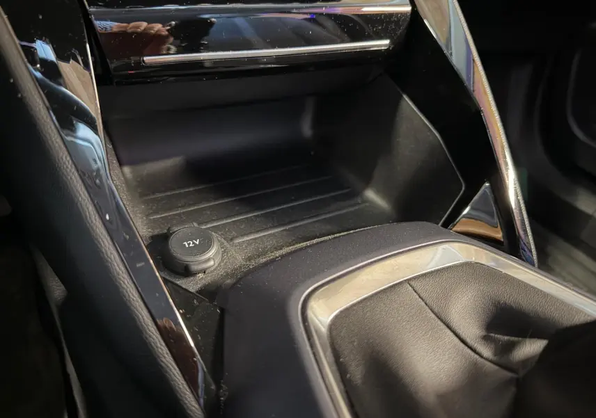 Gros plan de la console centrale noire du Peugeot 2008 1.5 BlueHDi 100 Allure avec prise 12V et habillage chromé.
